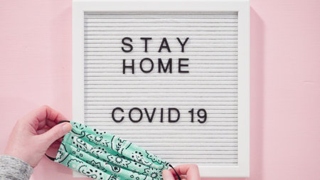 Flat lay. STAY HOME and COVID-19 sign on message board with a homemade face mask.