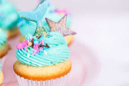Gourmet mermaid cupcakes topped with blue buttercream frosting and decorated with sprinkles and chocolate mermaid tails.の写真素材