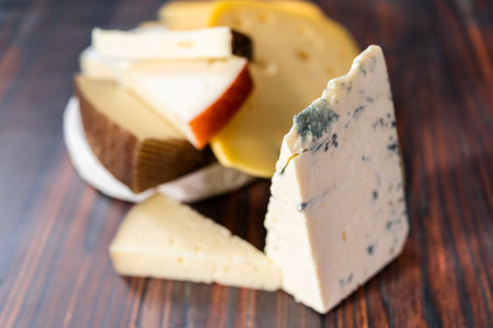 Variety of large gourmet cheese wedges on a dark wooden background.