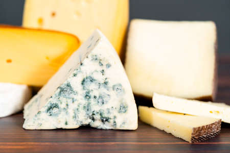 Variety of large gourmet cheese wedges on a dark wooden background.の写真素材