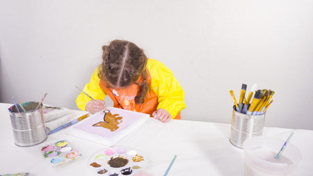 Little girl painting with acrylic paint on canvas with her mother for a distant learning art...