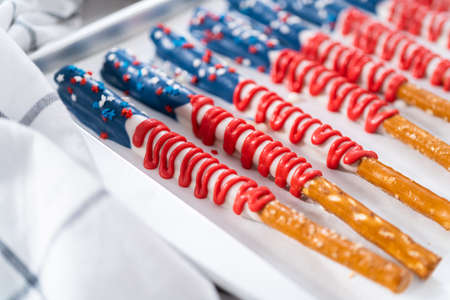 Homemade chocolate-covered pretzel rods decorated like the American flag drying on a baking sheet lined with parchment paper.の写真素材