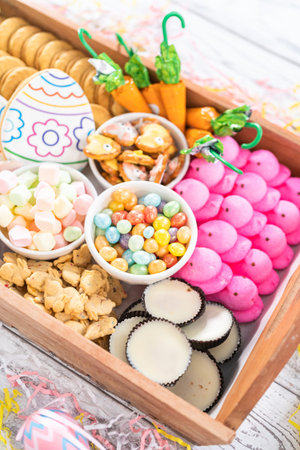 Assembling charcuterie board with Easter candies, cookies, and marshmallows.