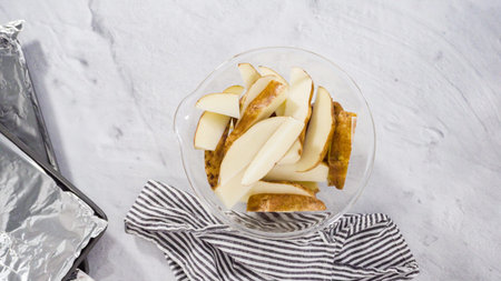 Flat lay. Step by step. Seasoning potato wedges in a bowl of water to prepare baked potato wedges...