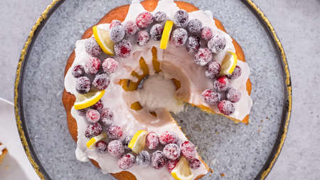 Flat lay. Step by step. Slicing lemon cranberry bundt cake decorated with sugar cranberries and lemon wedges.の写真素材