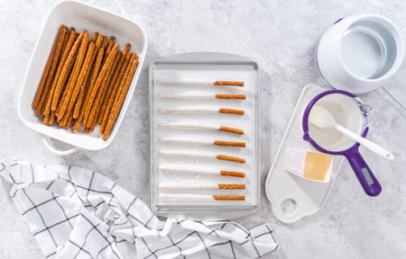 Flat lay. Dipping pretzel rods into the melted chocolate to prepare chocolate dipped pretzel rods...