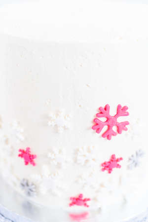 Frosting a tall round cake with white Italian buttercream icing and decorating with fondant snowflakes.の写真素材