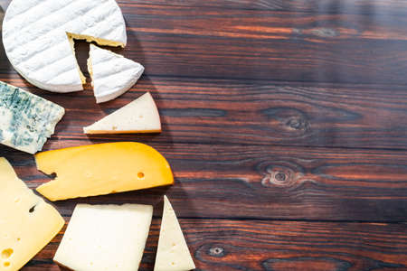 Flat lay. Variety of large gourmet cheese wedges on a dark wooden background.の写真素材