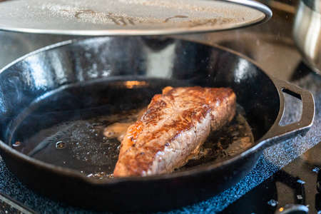 Frying New York strip steak in cast iron frying pan over the electric stove.の写真素材