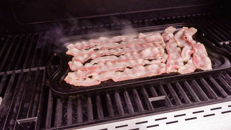 Cooking bacon stips on an outdoor gas grill.の写真素材