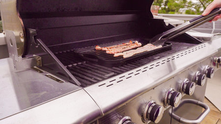 Cooking bacon stips on an outdoor gas grill.の写真素材