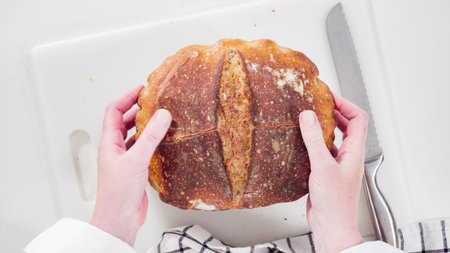 Flat lay. Slicing freshly baked sourdough wheat bread on a white cutting board.