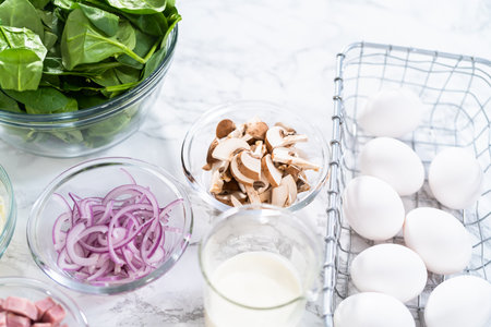 Ingredients in glass mixing bowls to prepare spinach and ham frittata.の写真素材