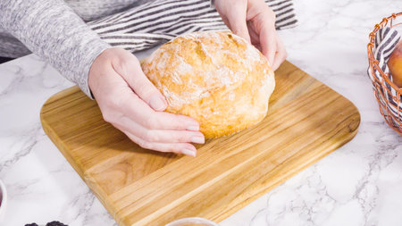 Step by step. Slicing a loaf of ciabatta bread with a bread knife on a wood cutting board.