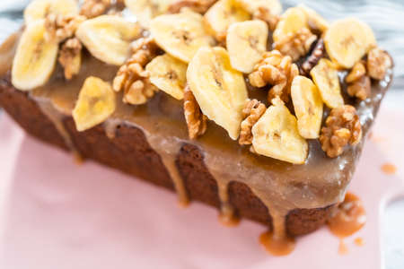 Freshly bakes a loaf of banana nut bread drizzled homemade caramel on a pink cutting board.の写真素材