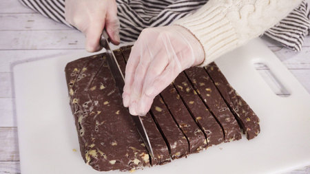 Step by step. Cutting homemade macadamia fudge on a white cutting board.