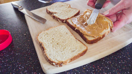 Preparing peanut butter and jelly sandwich on a wood cutting board.