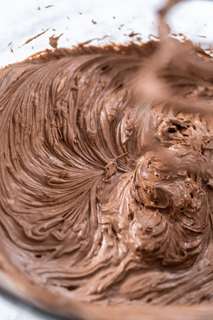 Mixing store-bought chocolate frosting in a mixing glass bowl with a hand mixer.
