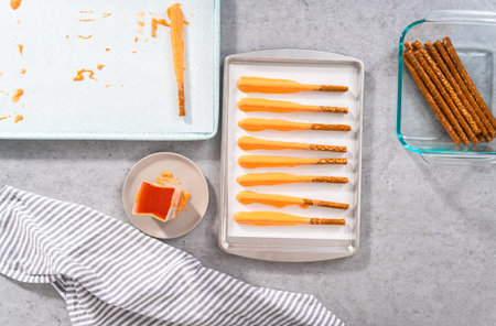 Flat lay. Dipping pretzel rods into melted chocolate to prepare carrot chocolate-covered pretzels.