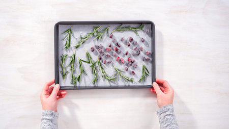 Step by step. Flat lay. Covering fresh cranberries and rosemary in sugar to decorate chocolate bundt...