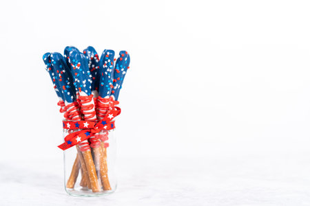 Homemade chocolate-covered pretzel rods decorated like the American flag in a glass jar.