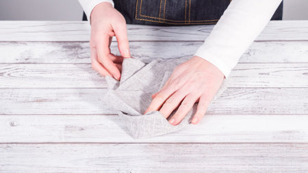 Step by step. Folding natural color linen dinner napkin on a wooden white table.