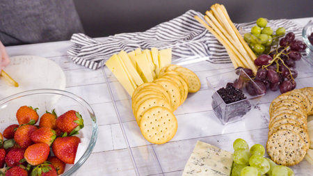 Step by step. Arranging cheese platter with fresh fruits, gourmet cheese, and crackers.