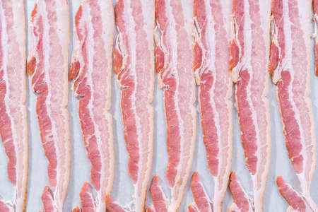 Uncooked bacon strips on a baking sheet with white parchment paper.の写真素材