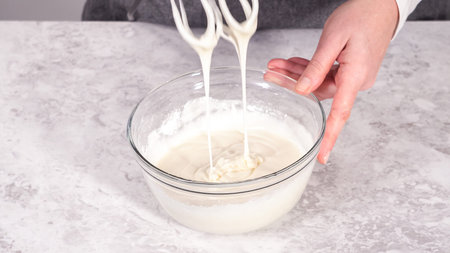 Step by step. Mixing ingredients in a glass mixing bowl to prepare cream cheese frosting.
