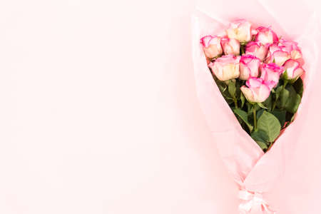 Flat lay. Bouquet of fresh pink roses wrapper in a pink paper on a pink background.の写真素材