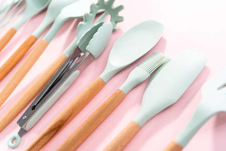 New blue silicone kitchen utensils with wooden handles on a pink background.の写真素材