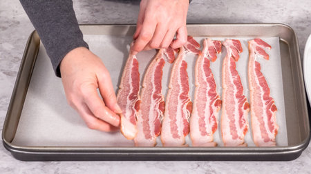 Step by step. Uncooked bacon strips on a baking sheet with white parchment paper.の写真素材