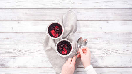 Step by step. Serving homemade mix berry compote in small white bowls on a wooden table.の写真素材