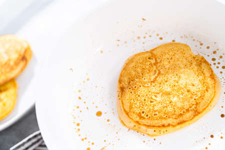 Frying pumpkin pancakes batter on a white frying pan.の写真素材