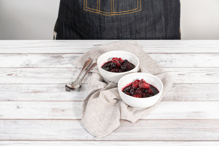 Homemade mix berry compote in small white bowls on a wooden table.の写真素材