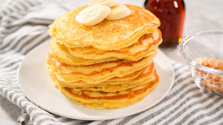 Step by step. Eating freshly baked coconut banana pancakes garnished with sliced bananas and toasted...