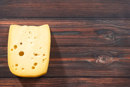 Flat lay. Large wedge of semi soft part-skim swiss cheese on a dark wooden background.