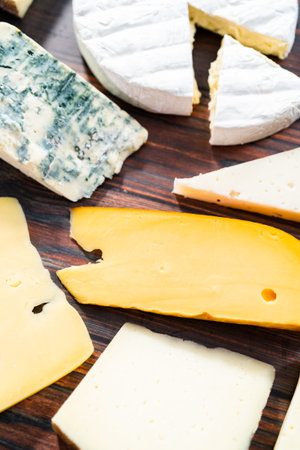 Variety of large gourmet cheese wedges on a dark wooden background.