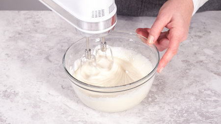 Step by step. Mixing ingredients in a glass mixing bowl to prepare cream cheese frosting.