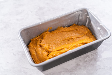 Pouring pumpkin bread batter into the greased loaf pan.