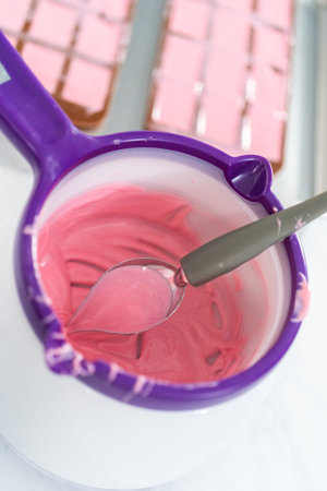 Filling silicone chocolate mold with melted chocolate to make mini pink chocolates.