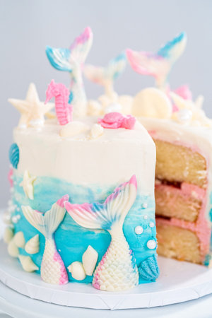 Slicing mermaid-themed 3 layer vanilla cake on a cake stand.
