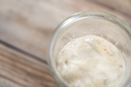 Feeding sourdough starter in a glass mason jar for baking artisan bread.