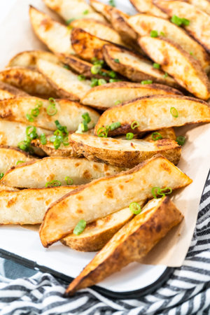 Freshly baked potato wedges with spices on a white serving tray.