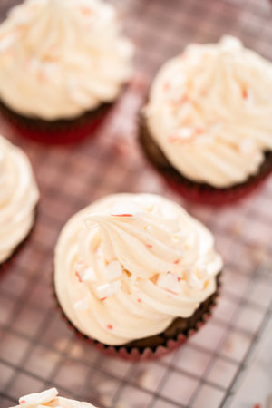 Piping peppermint buttercream frosting on top of the chocolate cupcakes and decorating with crushed...