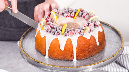 step by step. Slicing lemon cranberry bundt cake decorated with sugar cranberries and lemon wedges.