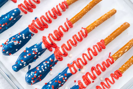 Homemade chocolate-covered pretzel rods decorated like the American flag drying on a baking sheet lined with parchment paper.の写真素材