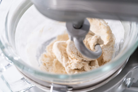 Mixing ingredients in a large glass mixing bowl to pizza dough.