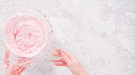 flat lay. step by step. Mixing in pink food coloring into a vanilla buttercream frosting for...