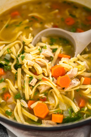 Serving chicken noodle soup with kluski noodles in white ceramic soup bowls.の写真素材